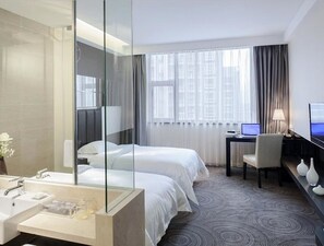 Une chambre d’hôtel avec un grand miroir, un lit, un bureau avec un ordinateur, une chaise et un téléviseur.