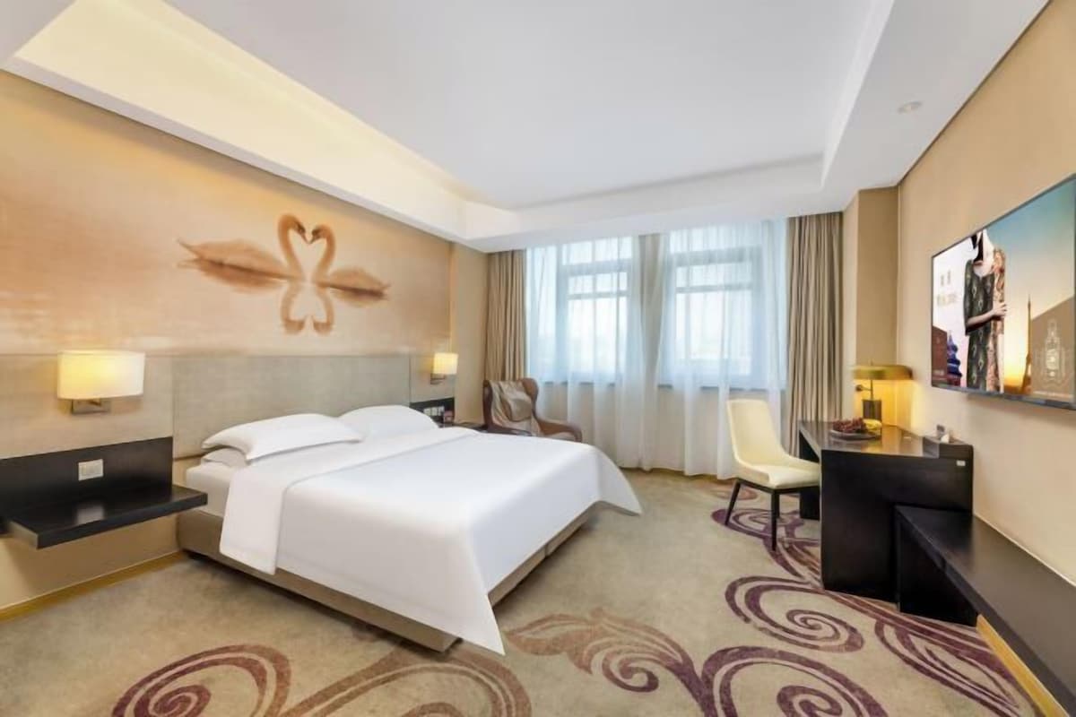 Une chambre d’hôtel avec un grand lit, un bureau, une chaise et un téléviseur fixé au mur.