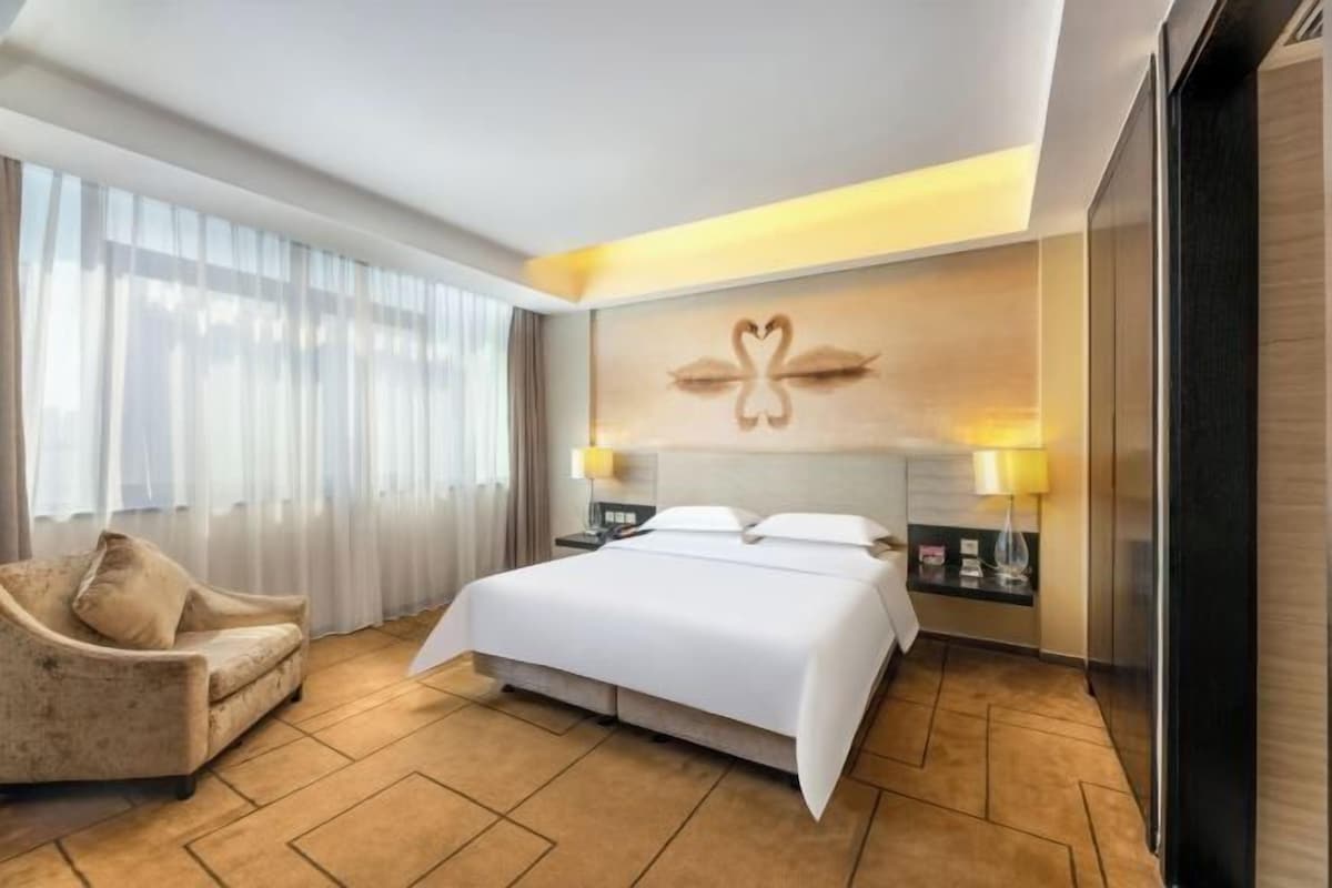 Une chambre d’hôtel moderne dotée d’un grand lit, d’un canapé, d’une œuvre d’art accrochée au mur et d’une table de chevet avec des lampes.