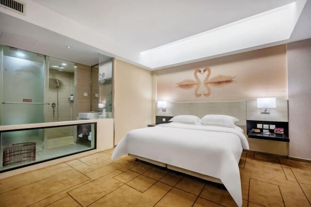 Une chambre d’hôtel moderne dotée d’un grand lit, d’une douche séparée par des parois en verre et d’un décor mural original.