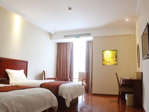 A hotel room with two beds, a desk, a chair, a trash bin, and a window with curtains.