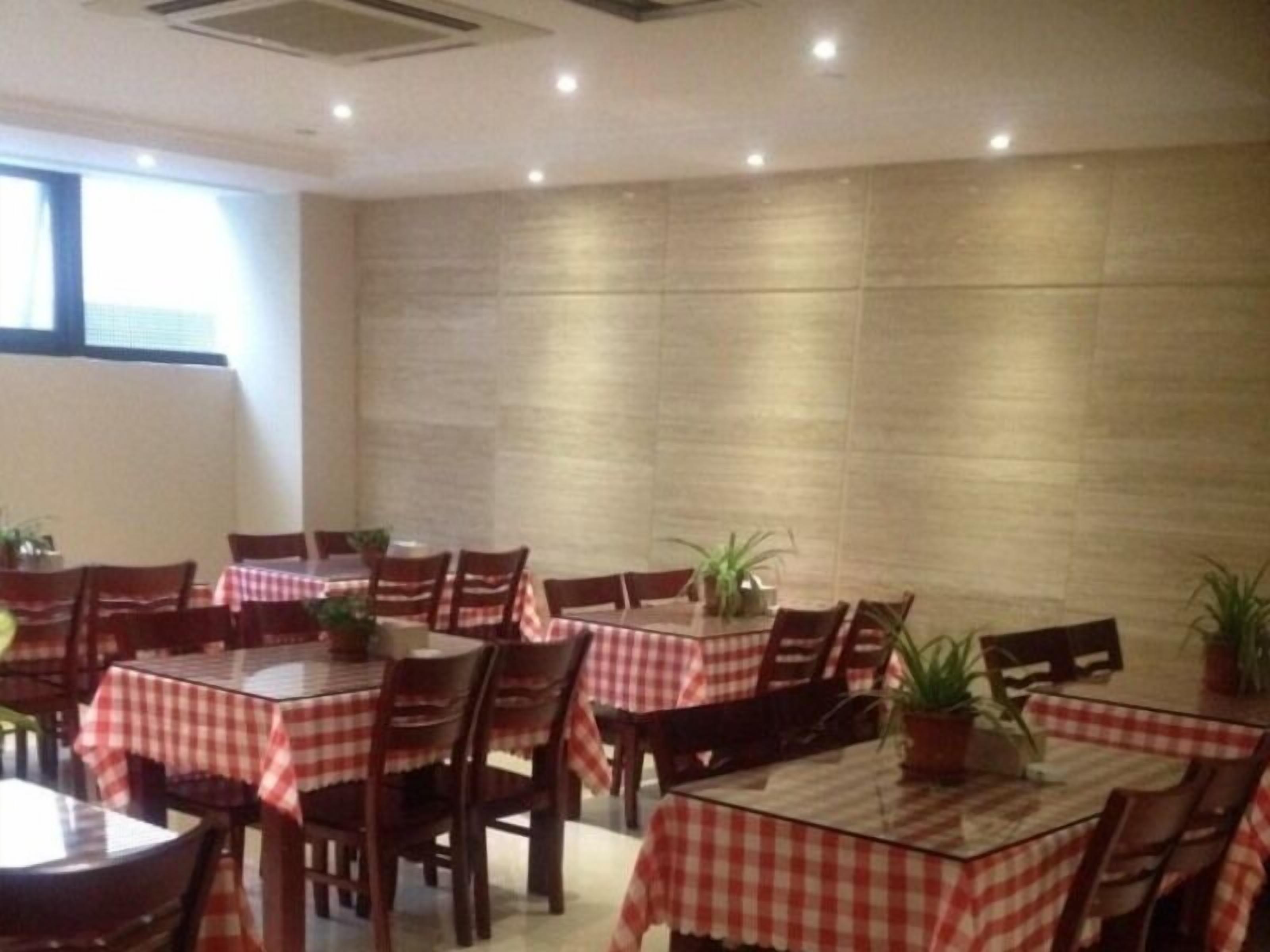 A dining area with multiple tables covered with red and white checkered tablecloths, wooden chairs, and potted plants.