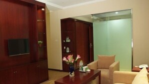 A hotel lobby with a wooden reception desk, beige sofas, a flat-screen TV mounted on the wall, and a green sliding door. - GreenTree Inn Zhoushan Putuo Donggang Hotel (Zhoushan)