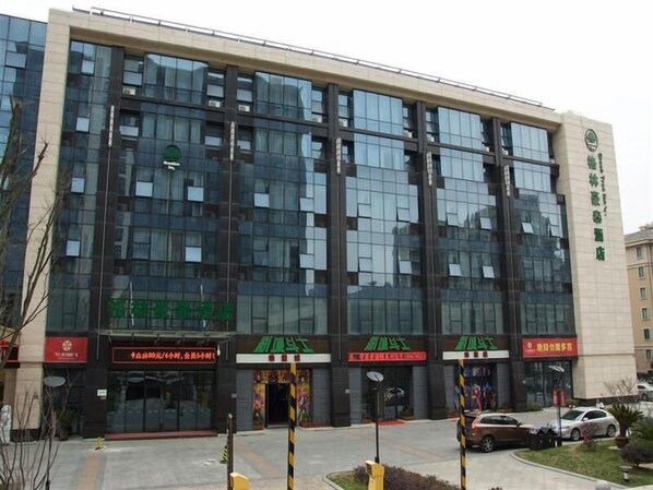 A modern building with multiple storefronts, including a green sign with white text, a red sign with white text, and a yellow sign with black text.