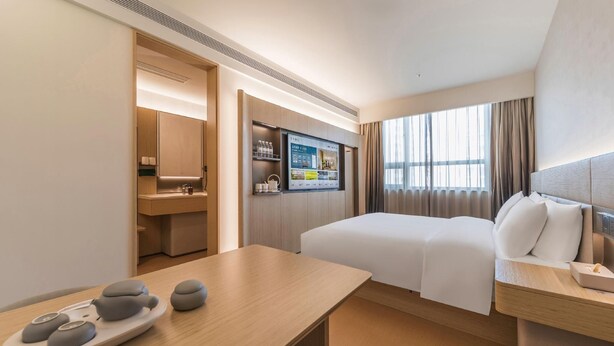 Ein Hotelzimmer mit Bett, Nachttisch, Schreibtisch mit Stuhl, Fernseher und einem Fenster mit Vorhängen.
