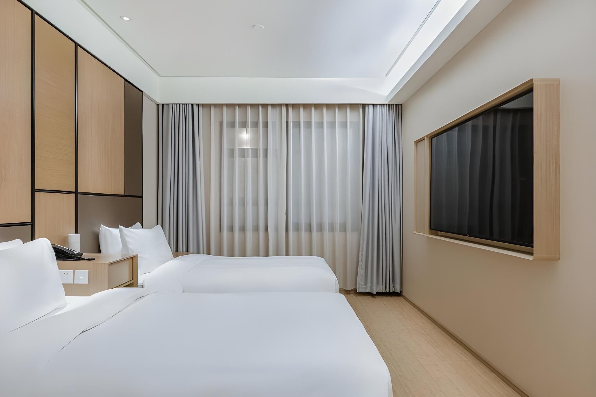 A hotel room with two beds, a desk, a phone, and a window with curtains.