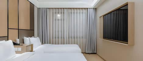 A hotel room with two beds, a desk, a phone, and a window with curtains.