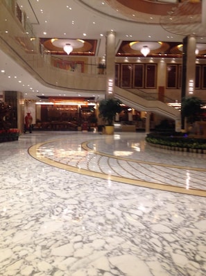 A spacious lobby with a marble floor, a central staircase, and a large chandelier.
