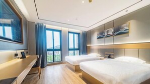 Una habitación de hotel moderna con suelo de madera, dos camas individuales, un escritorio y un ventanal con cortinas.