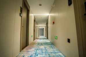 A hotel hallway with a patterned carpet, doors on both sides, and emergency exit signs. - Doukou Lijing Hotel (Nanling) (Wuhu)