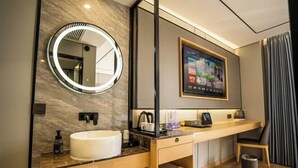 Un baño moderno con un espejo redondo, lavamanos y un cuadro enmarcado sobre el mueble.