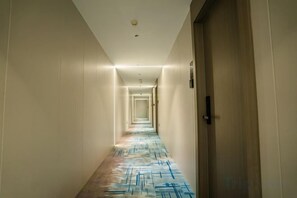 Un pasillo de hotel con alfombra estampada, puertas a ambos lados y una lámpara en el techo.