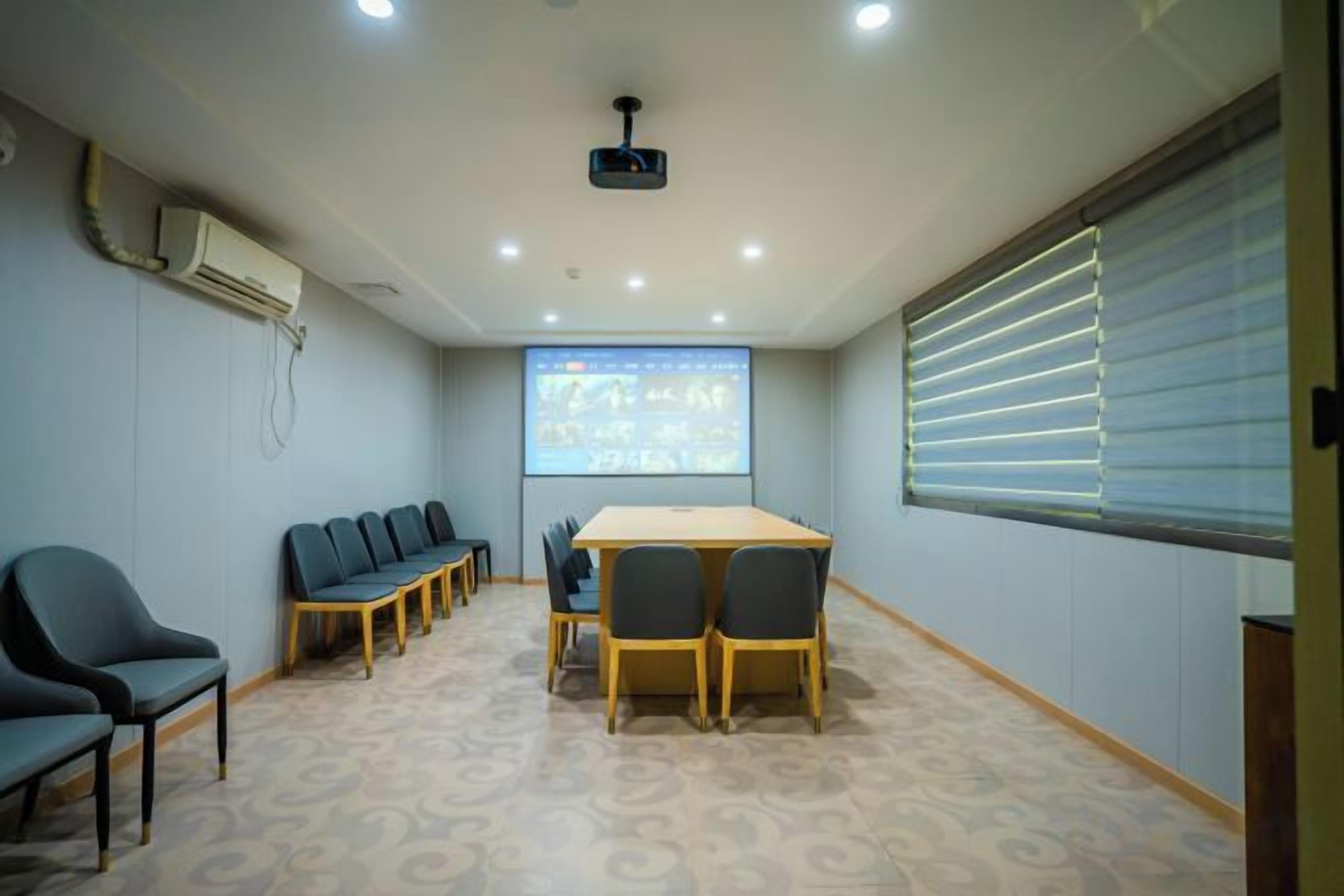 A conference room with a large table, chairs, a projector screen, and a window with blinds.
