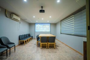 Un salón de conferencias con una gran mesa, sillas, una pantalla de proyector y un ventanal con persianas.