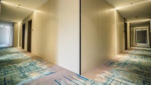 Pasillo de hotel con alfombra estampada, iluminación empotrada y puertas que dan a habitaciones.