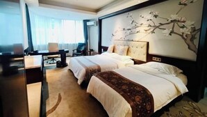 Ein Hotelzimmer mit zwei Betten, einem Schreibtisch, einem Stuhl und einem großen Blumenfries an der Wand.