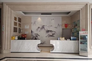 Una recepción con mostrador de mármol, certificados enmarcados y una obra de arte tradicional en la pared.