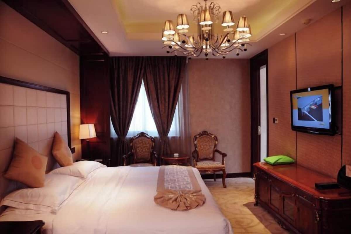 A hotel room with a large bed, two chairs, a TV, and a chandelier.