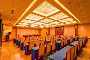 Ein Konferenzraum mit Tischen und Stühlen, einem großen Bildschirm und einer Decke mit einer geometrischen Leuchte.