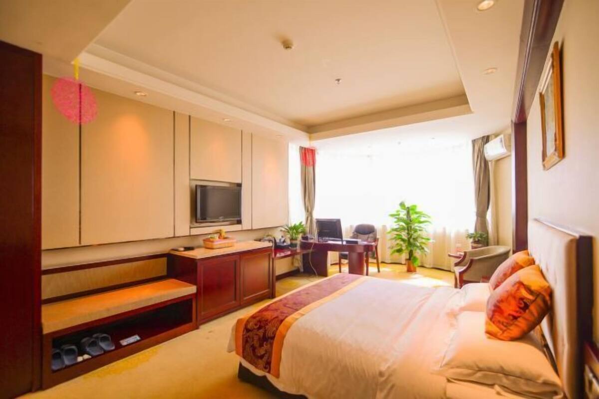 A hotel room with a bed, a desk, a TV, and a window with curtains.
