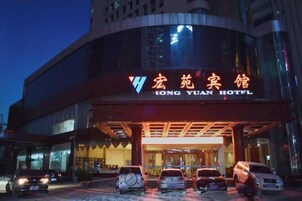 Exterior del hotel Hong Yuan con un diseño moderno, destacando una entrada principal y varios coches aparcados delante.