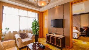 Ein Hotelzimmer mit einer Couch, einem Couchtisch, einem Fernseher, einer Pflanze und einem Bett.
