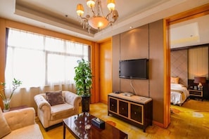 A hotel room with a sofa, a coffee table, a TV, a plant, and a bed. - Hongyuan Hotel (Shijiazhuang)