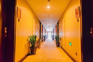 Un pasillo de hotel con puertas a ambos lados, plantas en macetas y suelo alfombrado.