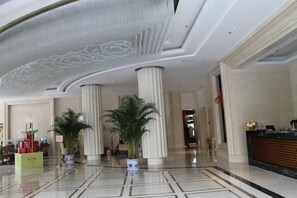 Un vestíbulo con suelo de mármol, amplias columnas y una mesa de recepción.