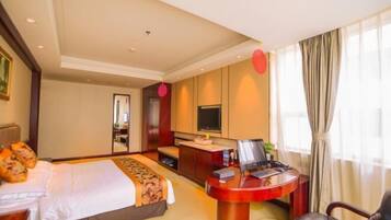 A hotel room with a bed, a desk, a chair, a TV, and a window with curtains.