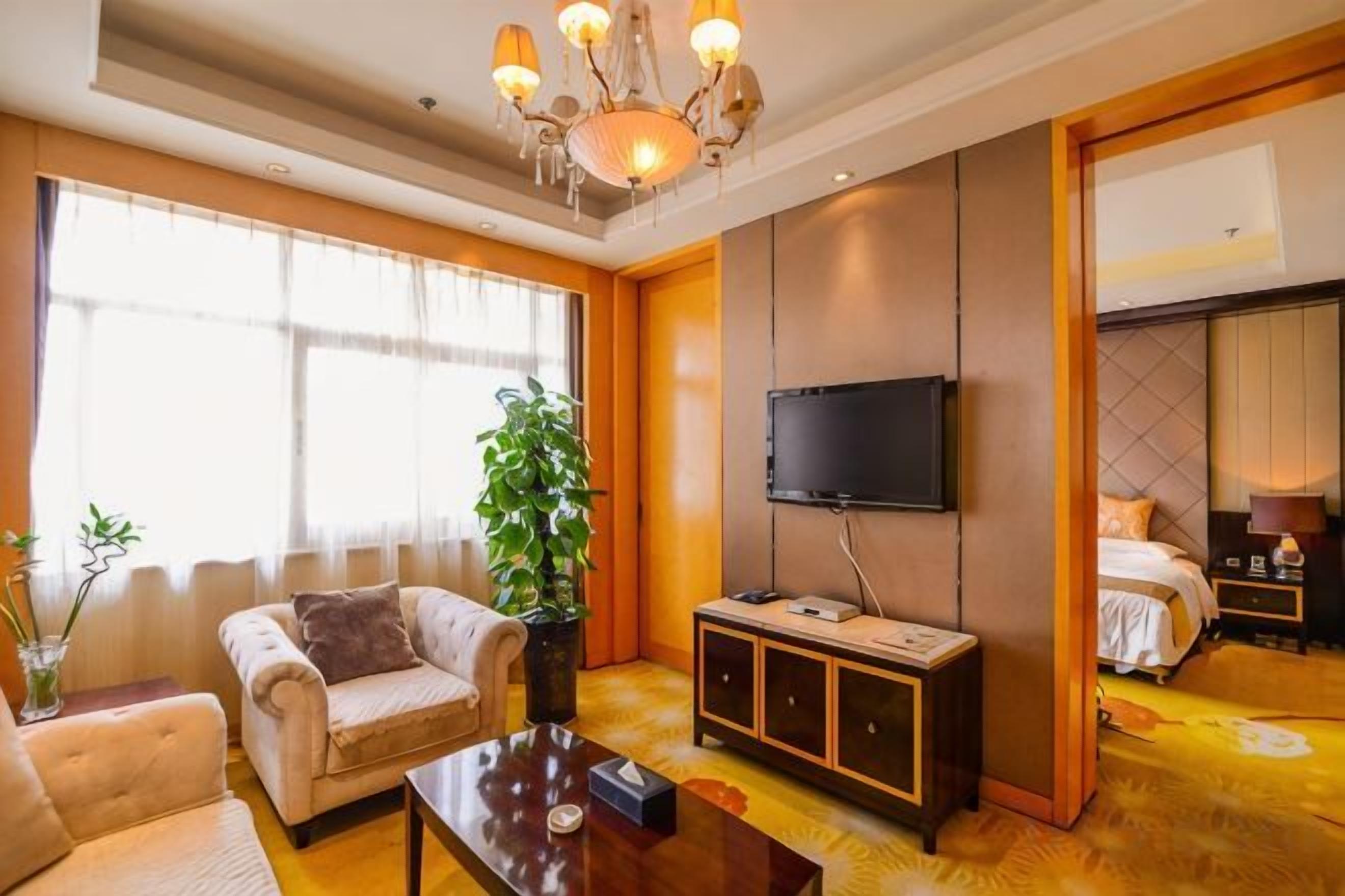 A hotel room with a sofa, a television, a cabinet, and a large window.