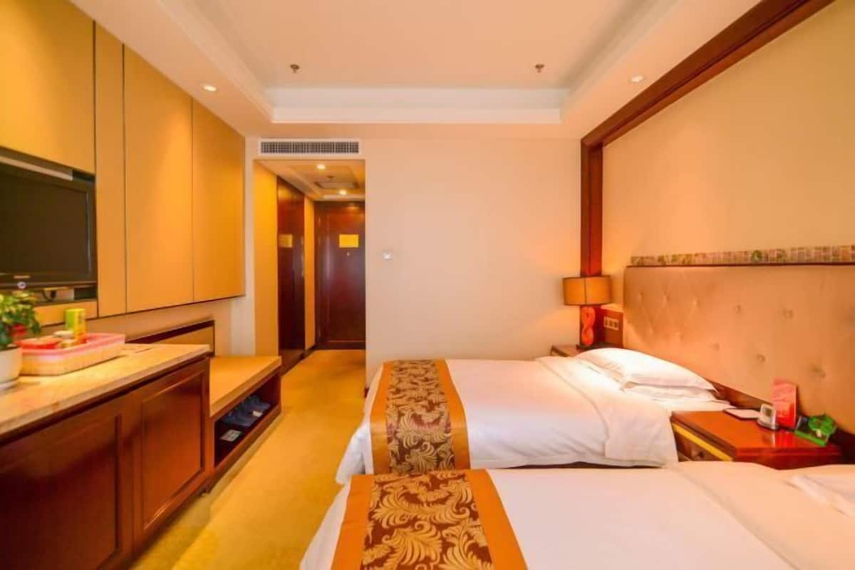 A hotel room with two beds, a TV, a desk, and a bathroom visible through an open door.
