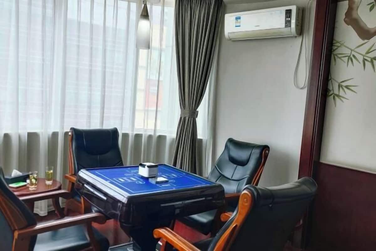 A room with a blue table, four chairs, a radiator, an air conditioner, and a window with curtains.
