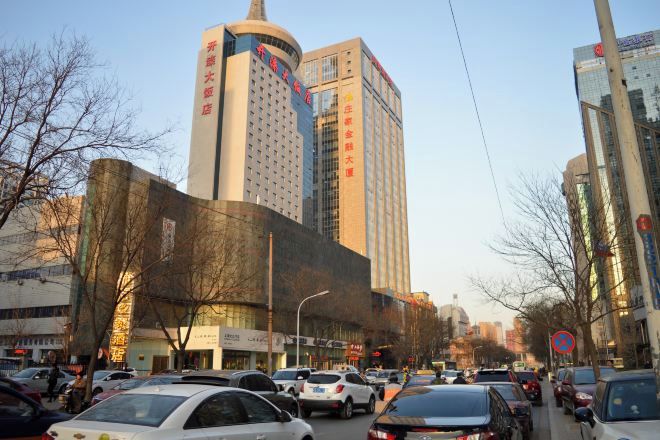 Un edificio de varios pisos con señalización que indica servicios de hotel, rodeado de coches aparcados y árboles.