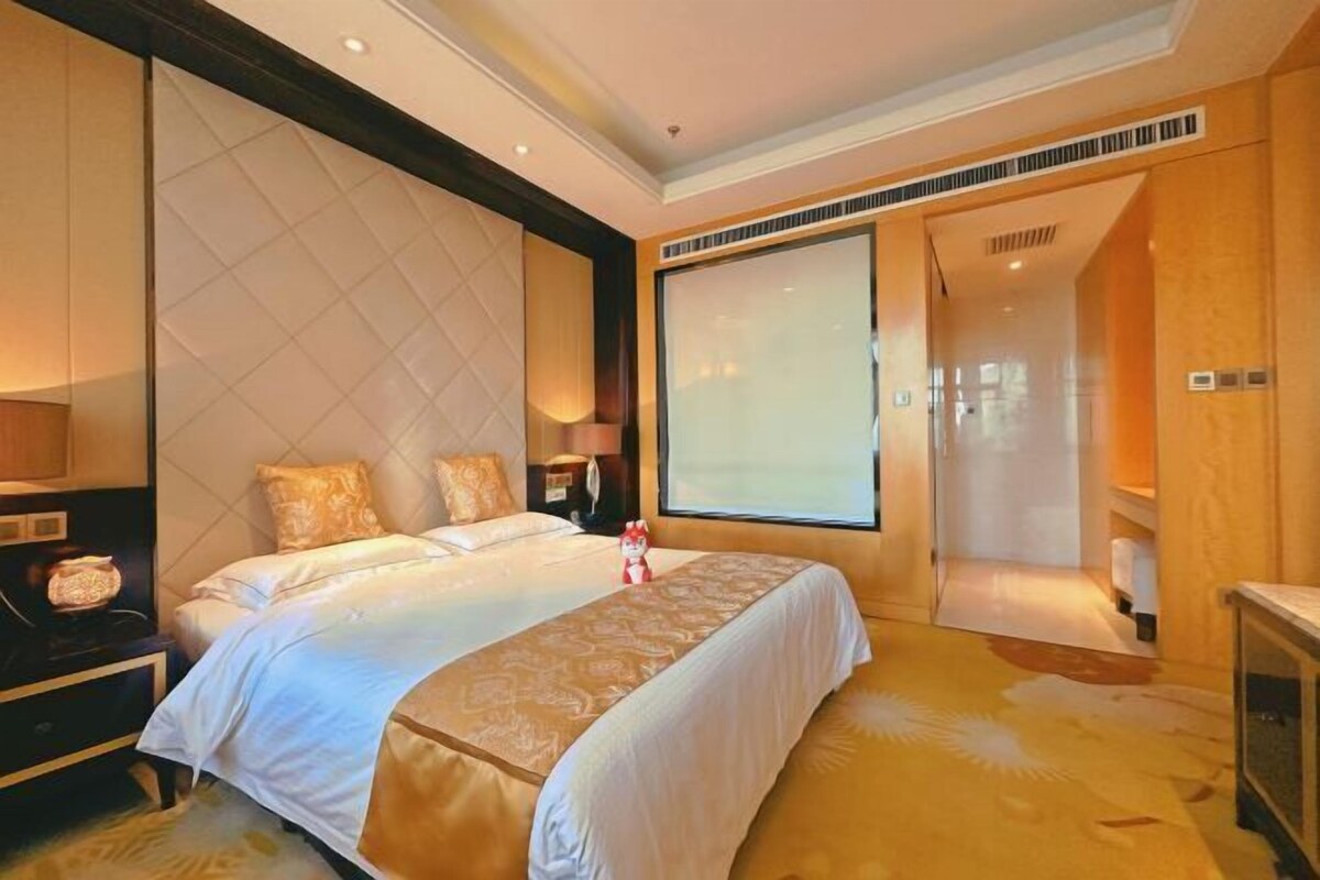 Een hotelkamer met een groot bed, een nachtkastje, een lamp, een raam en een deur naar een badkamer.