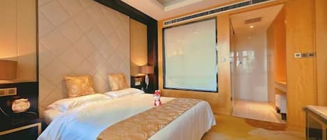 A hotel room with a large bed, a nightstand, a lamp, a window, and a door leading to a bathroom.