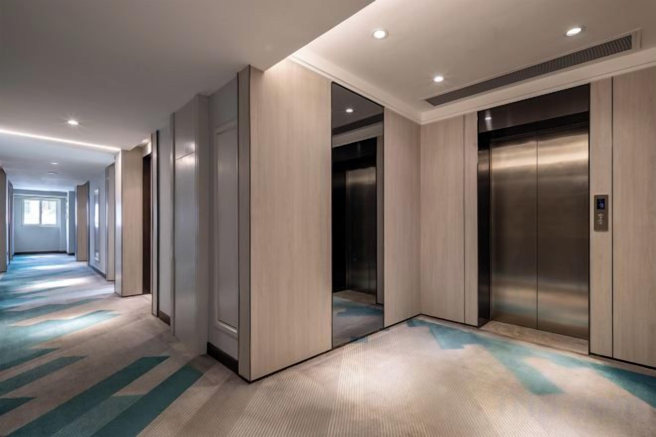 Un pasillo de hotel con dos ascensores, suelo alfombrado y una larga galería.