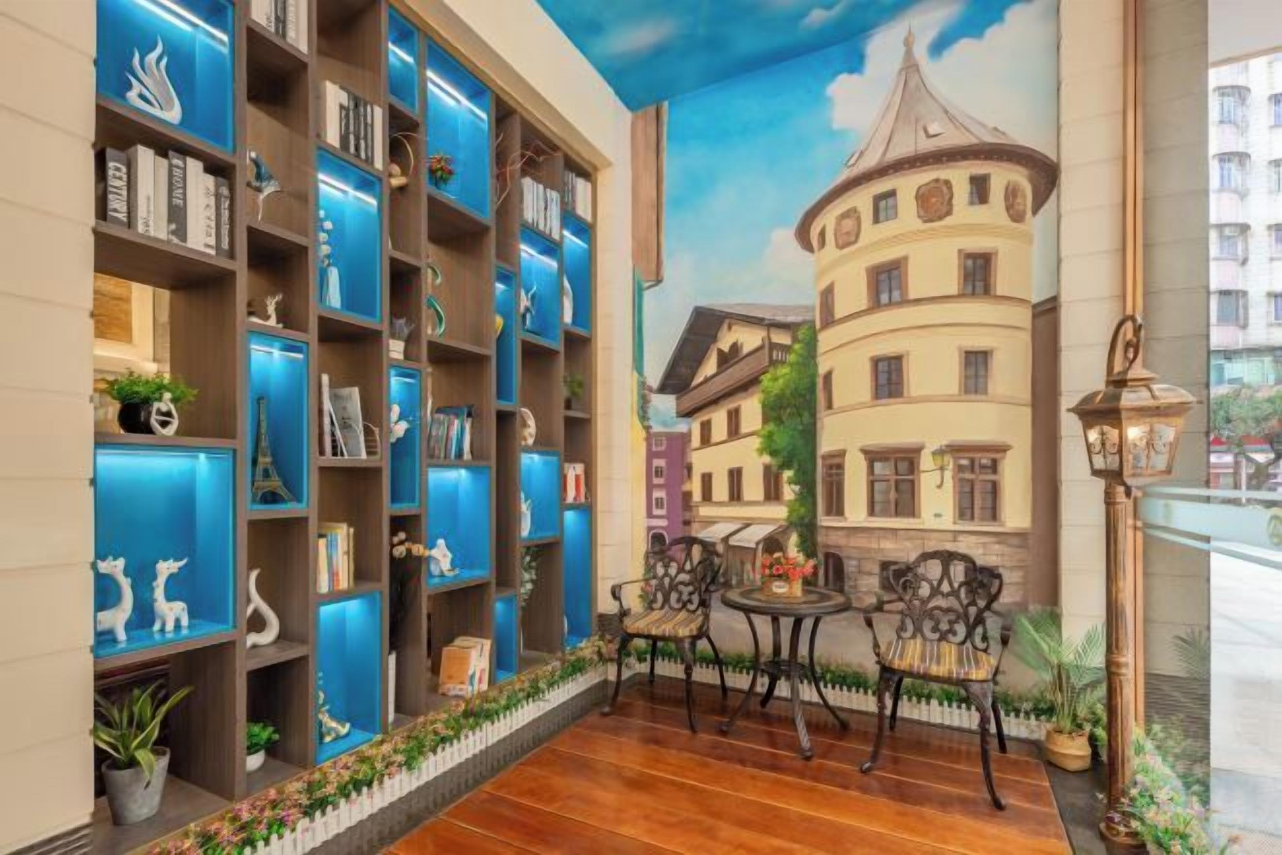 Zona d'estar interior acollidora amb un mural d'una ciutat europea, una estanteria amb objectes decoratius i una taula petita amb cadires.