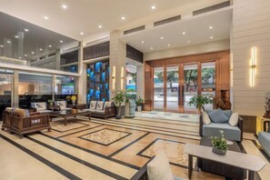 Un vestíbulo amplio con zona de estar, televisor y mostrador de recepción.
