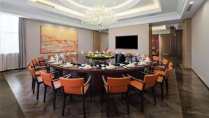 Un salón de conferencias con una mesa redonda, sillas naranjas, un candelabro y un cuadro grande en la pared.