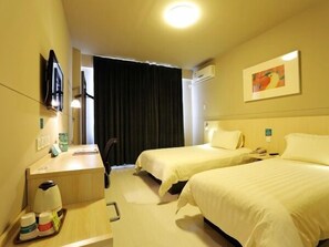 A hotel room with two beds, a desk with a coffee maker, a TV, and an air conditioning unit.