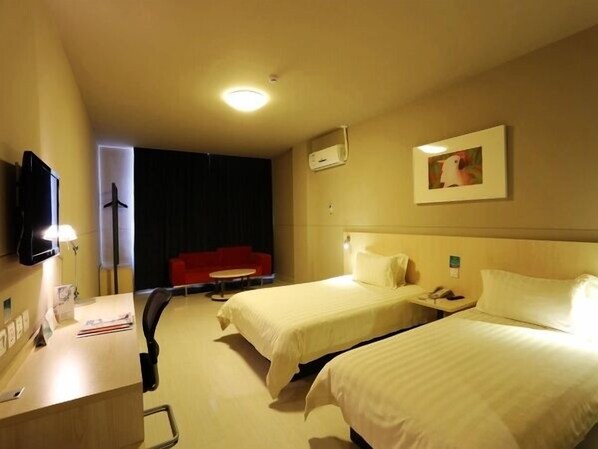 A hotel room with two beds, a desk, a television, and a red couch.