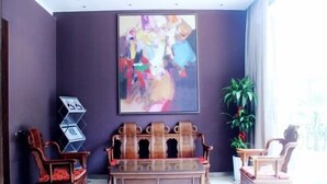 A room with a large abstract painting, a wooden bench, two wooden chairs, and a potted plant. - Jinjiang Inn Xiamen Hexiang Road West (Xiamen)