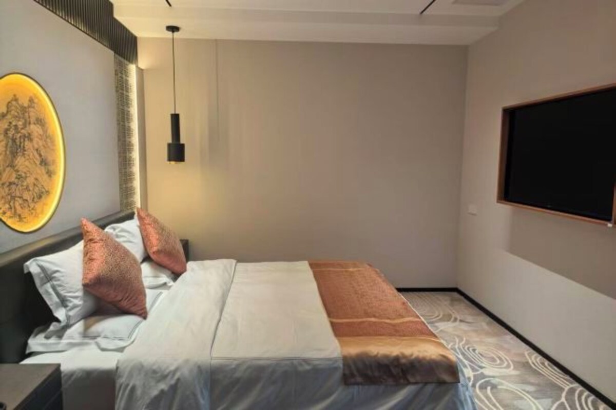 Hotelkamer met een bed, een aan de muur hangend kunstwerk, een hanglamp en een raam met uitzicht.