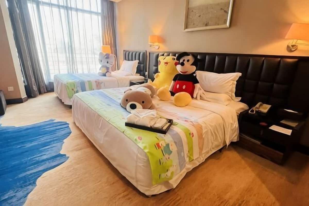 Une chambre d’hôtel avec deux lits, des peluches, une table de chevet et une lampe.