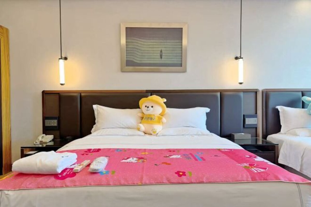 Een hotelkamer met een bed, nachtkastje, lamp en een zacht knuffeldiertje.