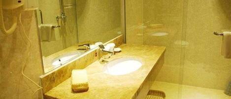 Baño con lavamanos de mármol, espejo, cabezal de ducha de mano y perchero para toallas.