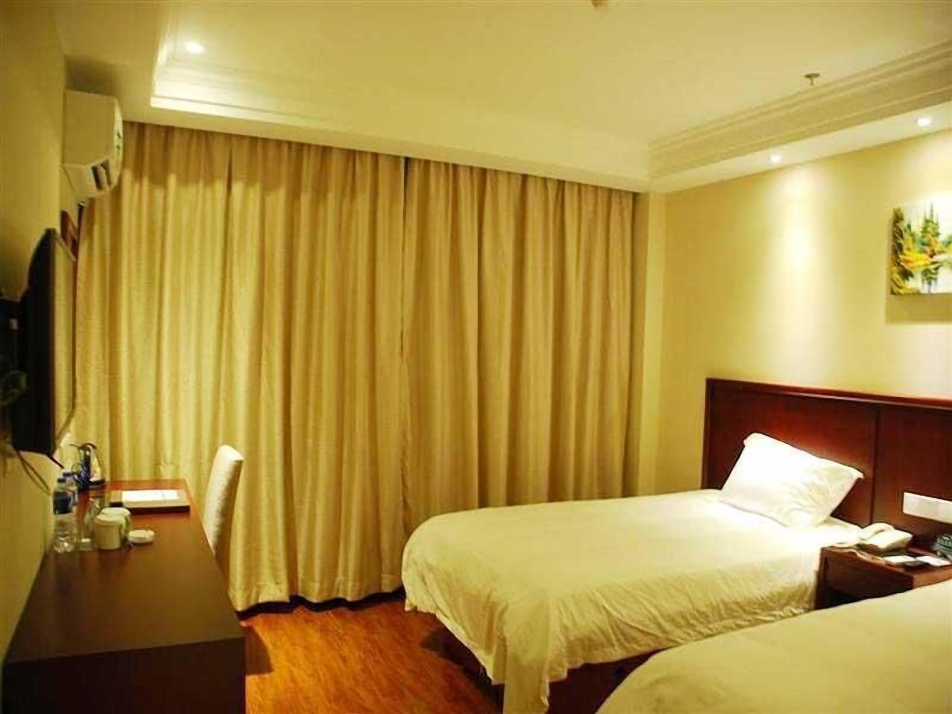 A hotel room with two beds, a wooden desk, a chair, and a large window with curtains.