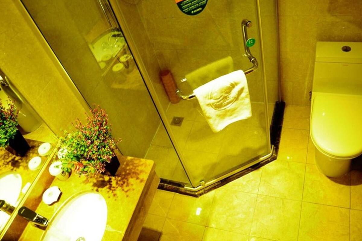 A bathroom with a glass shower door, a toilet, and a sink with a towel hanging on the door.