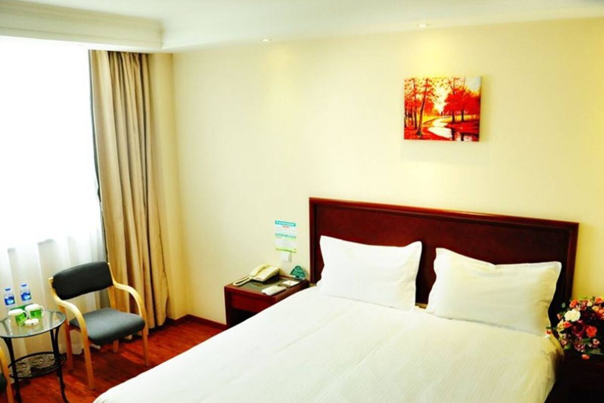 A hotel room with a large bed, a desk with a chair, a telephone, and a painting on the wall.
